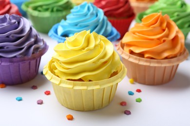 Photo of Many tasty cupcakes with bright cream and sprinkles on white background, closeup