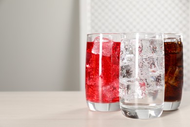 Photo of Glasses of different refreshing soda water with ice cubes on white table, space for text
