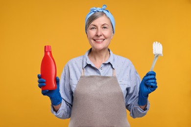 Happy housewife bottle of detergent and brush on orange background