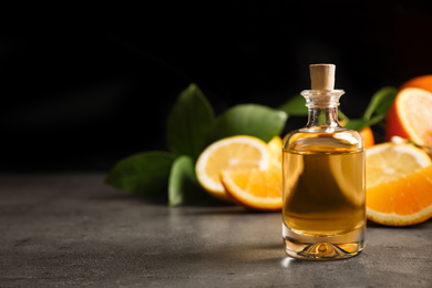 Photo of Bottle of essential oil and citrus fruits on grey table. Space for text