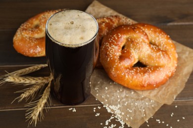 Photo of Tasty pretzels, glass of beer and wheat spikes on wooden table