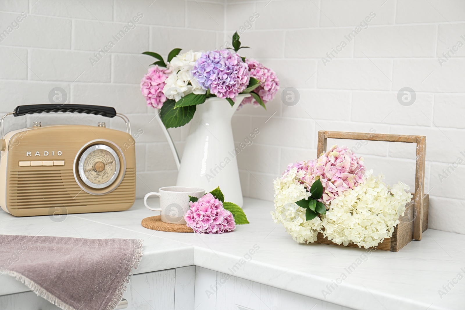 Photo of Beautiful hydrangea flowers, cup and radio set on light countertop