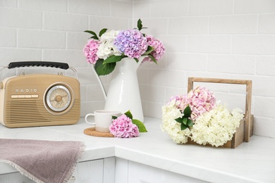 Beautiful hydrangea flowers, cup and radio set on light countertop