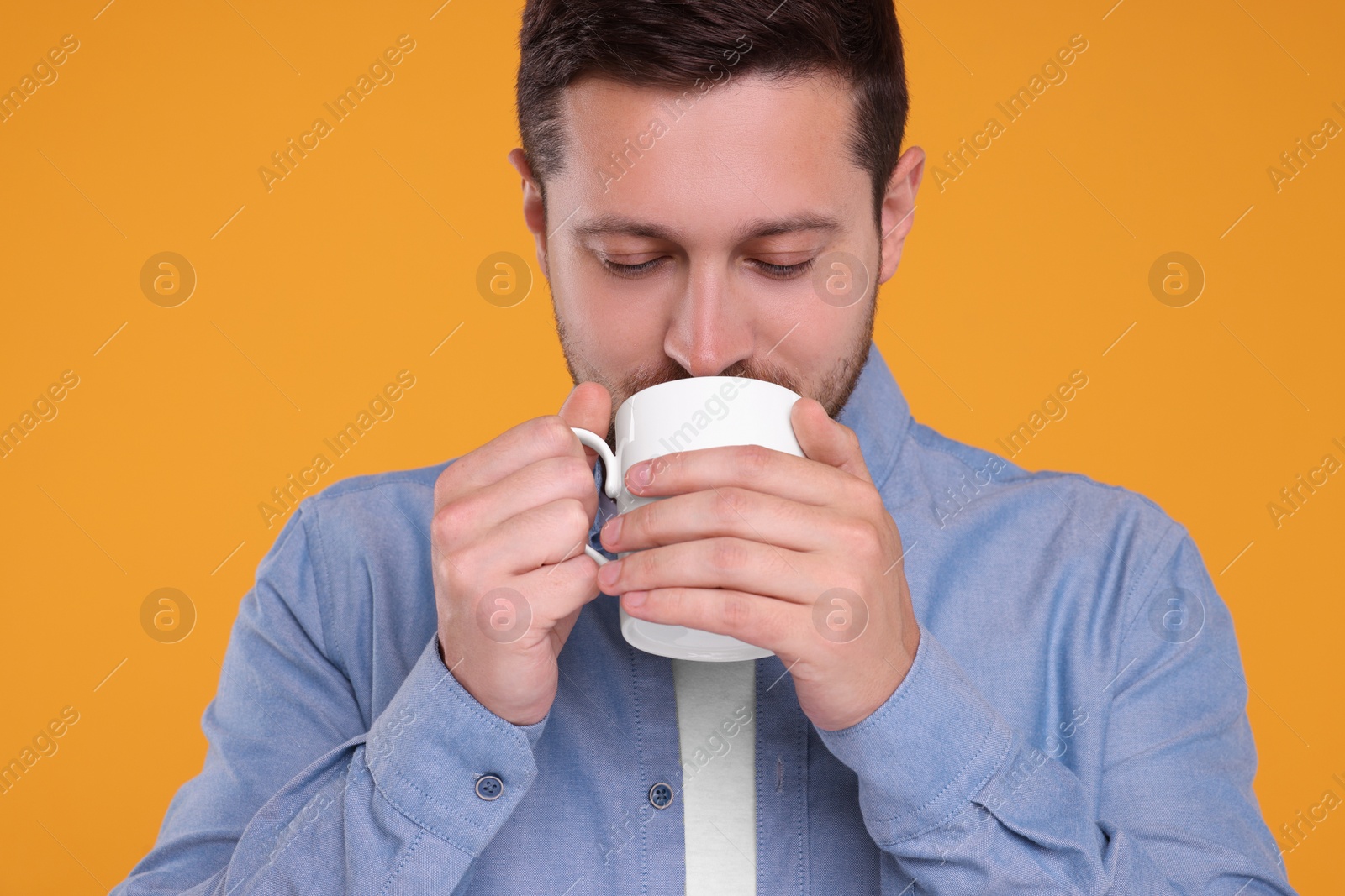 Photo of Man drinking from white mug on orange background