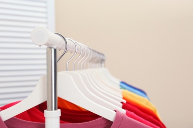 Photo of Rack with bright clothes in room. Rainbow colors