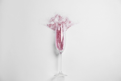 Photo of Champagne glass with pink glitter on white background, top view. Hilarious celebration