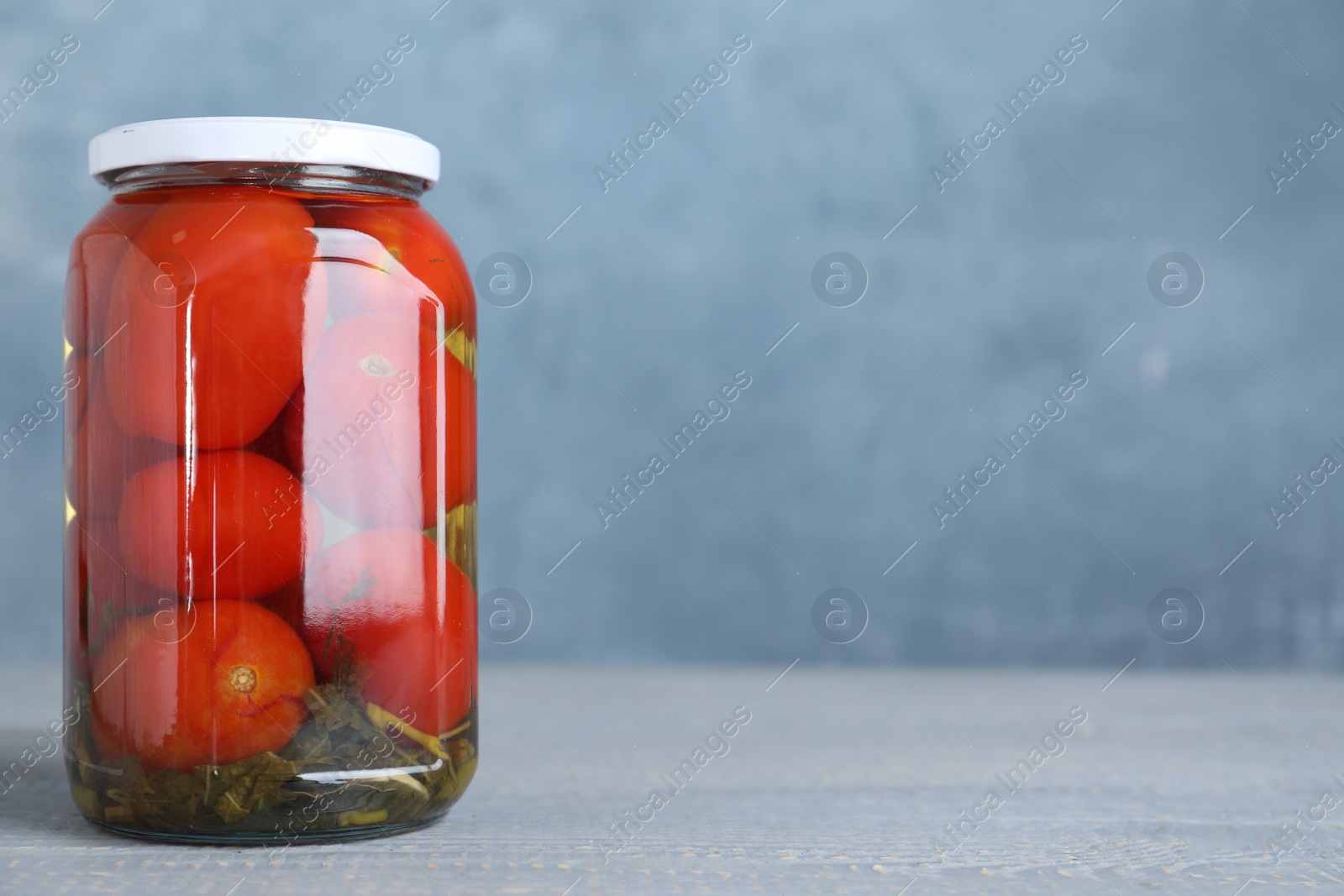 Photo of Glass jar with pickled tomatoes on table. Space for text