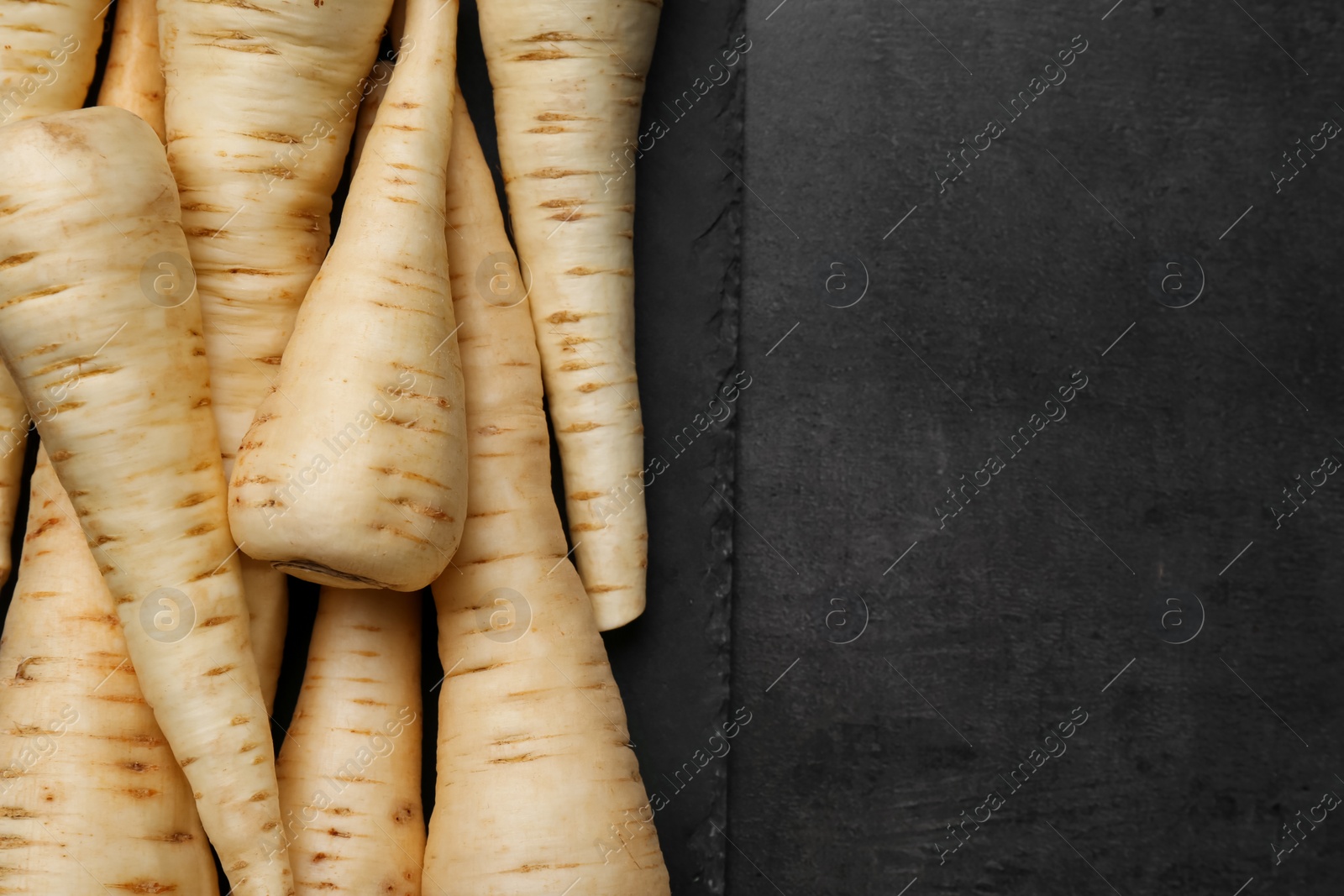 Photo of Delicious fresh ripe parsnips on black table, top view. Space for text