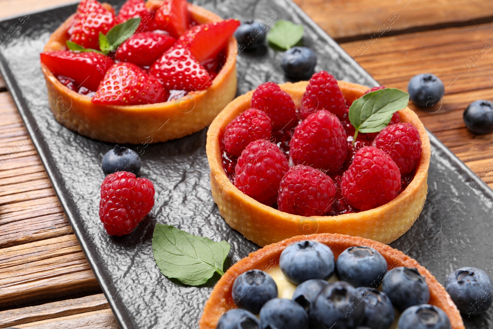 Photo of Tartlets with different fresh berries on wooden table, closeup. Delicious dessert