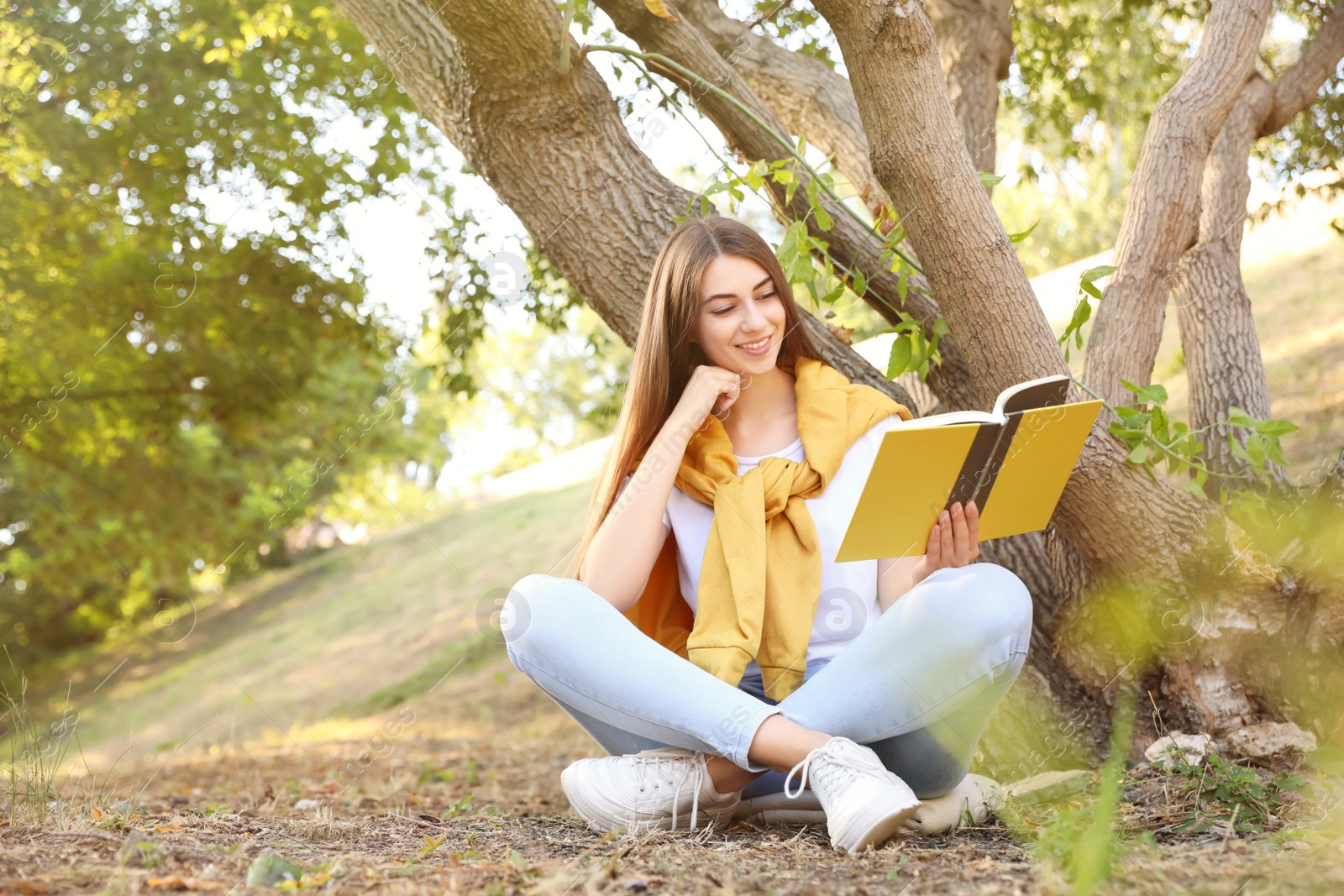Photo of Young woman reading book near tree in park