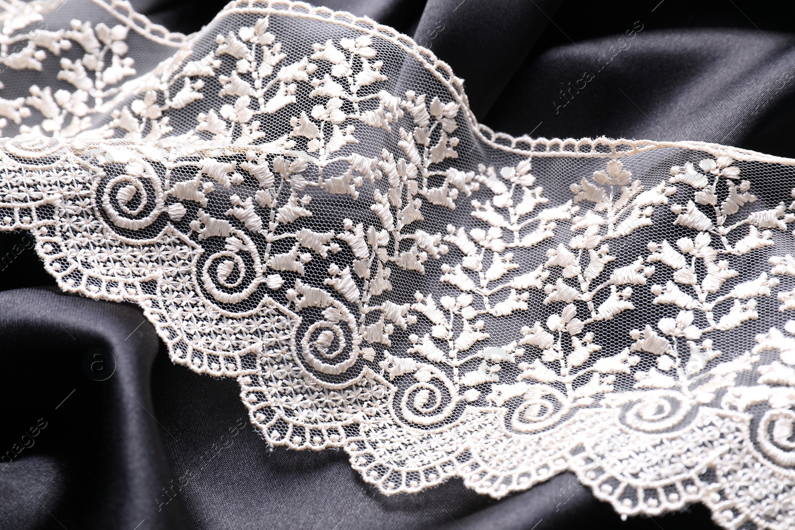 Photo of Beautiful white lace on black fabric, closeup