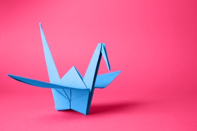Photo of Origami art. Handmade paper crane on pink background, closeup. Space for text