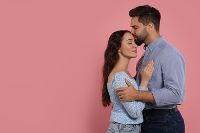 Photo of Man kissing his girlfriend on pink background. Space for text