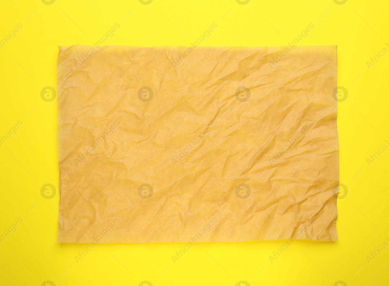 Photo of Sheet of crumpled brown baking paper on yellow background, top view