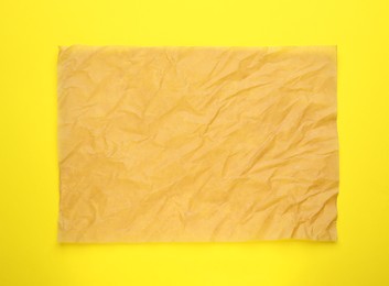 Sheet of crumpled brown baking paper on yellow background, top view