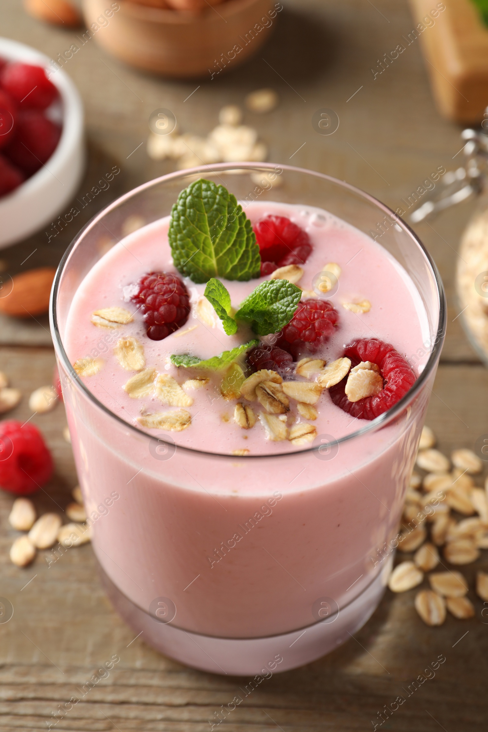 Photo of Glass of tasty raspberry smoothie with oatmeal and mint on wooden table