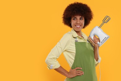 Photo of Happy young woman in apron holding mixer on orange background. Space for text