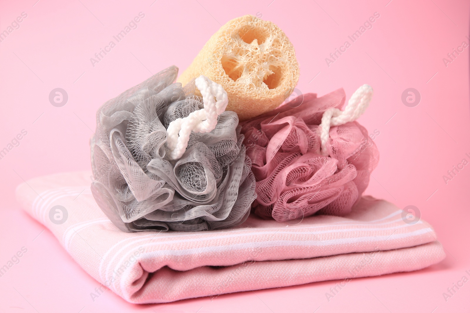 Photo of Colorful shower puffs, loofah sponge and towel on pink background