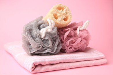 Colorful shower puffs, loofah sponge and towel on pink background