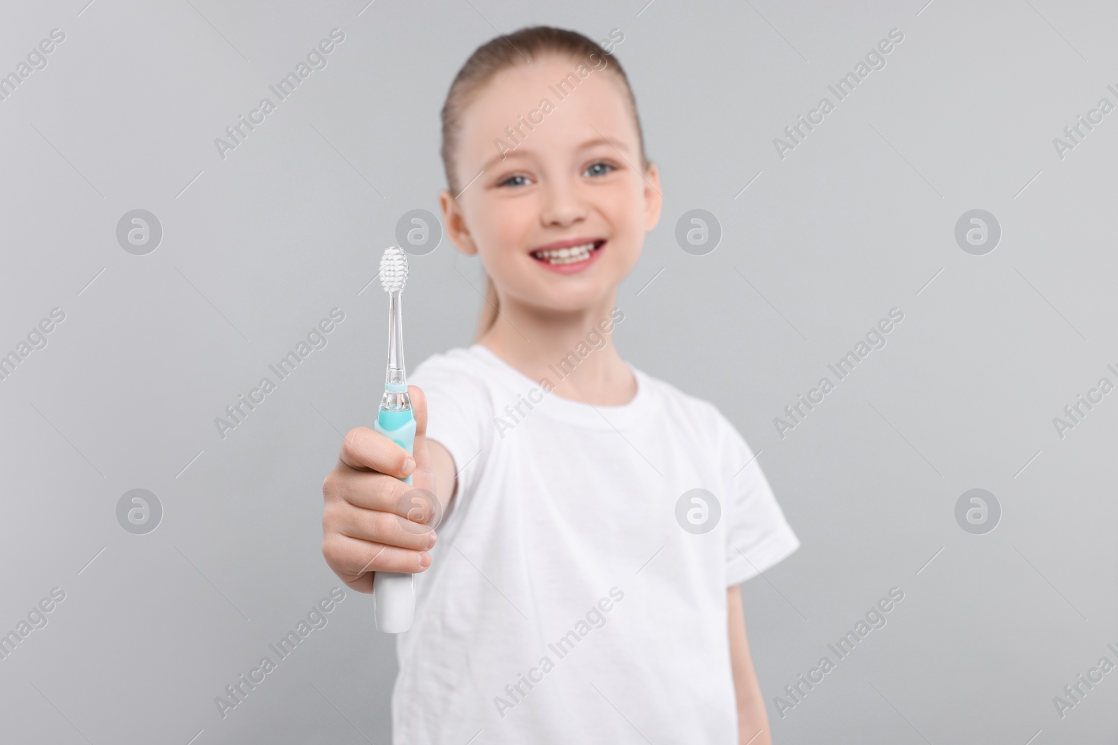 Photo of Happy girl holding electric toothbrush on light grey background, selective focus