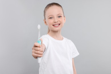 Photo of Happy girl holding electric toothbrush on light grey background, selective focus