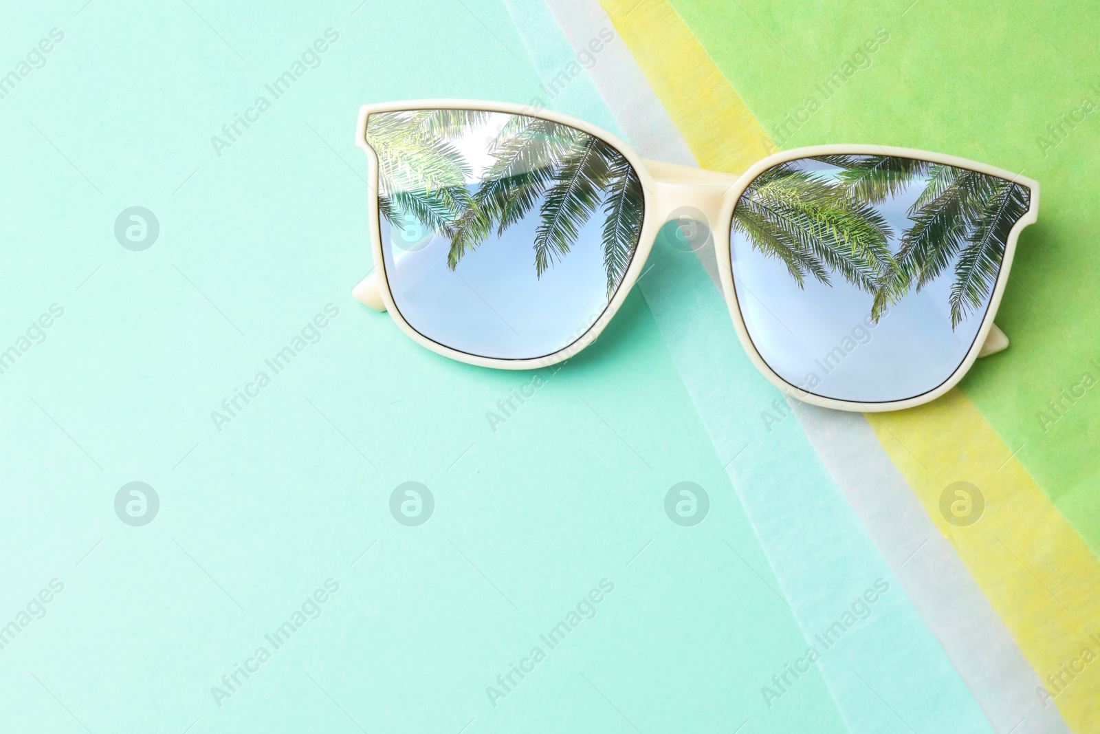 Image of Stylish sunglasses on color background, top view. Sky and palm trees reflecting in lenses