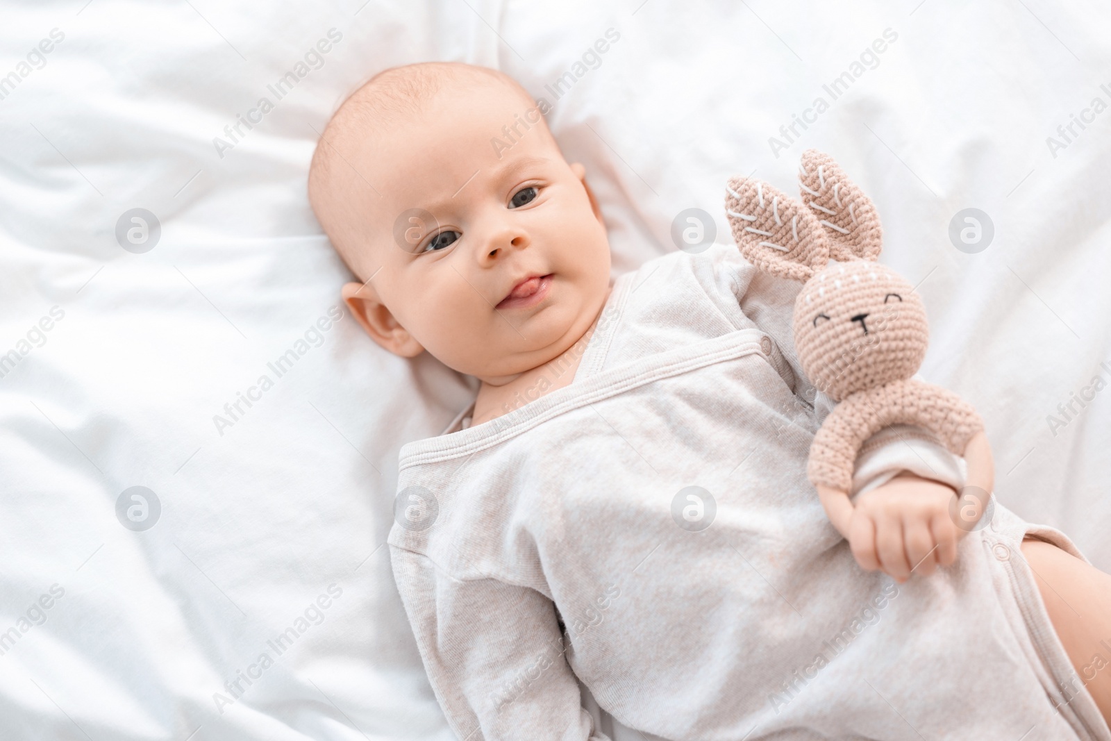Photo of Cute little baby with toy lying on white sheets, top view