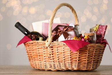 Photo of Wicker basket with gifts, wine and food against blurred festive lights. Space for text