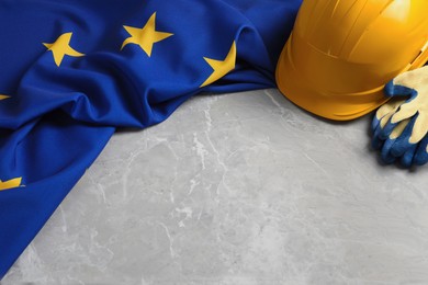 Photo of European Union flag, yellow hard hat and gloves on grey marble table, space for text