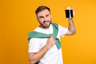 Photo of Handsome man with cold kvass on yellow background. Traditional Russian summer drink