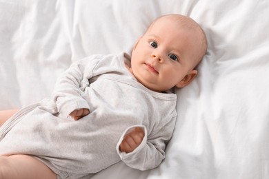 Photo of Cute little baby lying on white sheets, top view