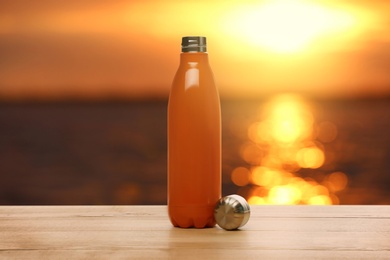 Thermo bottle on wooden table near sea at sunset