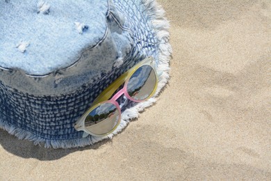 Jeans hat and sunglasses on sand, above view with space for text. Beach accessories