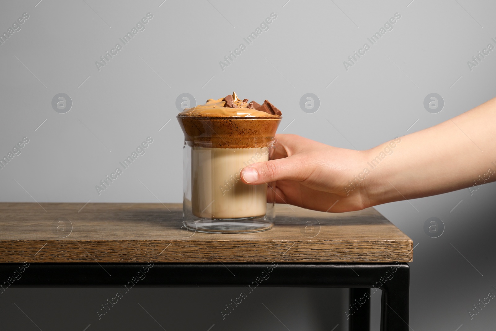 Photo of Woman taking glass of delicious dalgona coffee with chocolate from wooden table, closeup