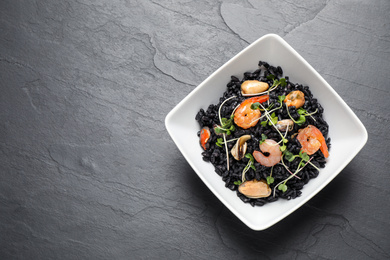 Photo of Delicious black risotto with seafood in bowl on grey table, top view. Space for text