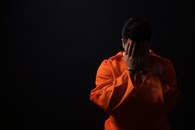 Photo of Prisoner in jumpsuit with handcuffs on black background, space for text