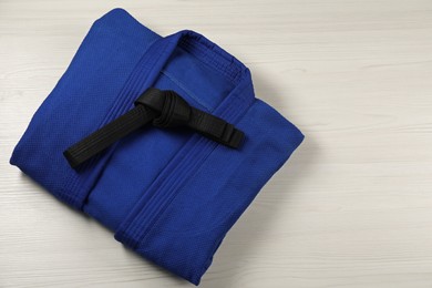 Photo of Black karate belt and blue kimono on wooden background, top view. Space for text