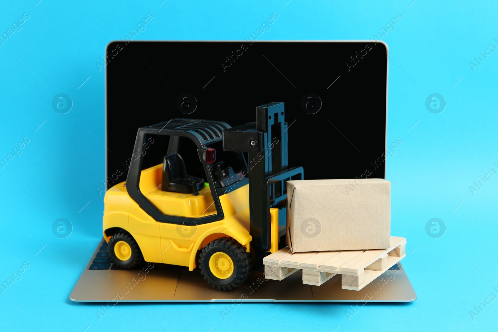 Photo of Laptop, toy forklift with wooden pallet and box on light blue background