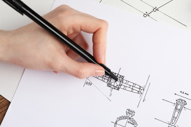 Photo of Jeweler drawing sketch of elegant ring on paper at wooden table, closeup