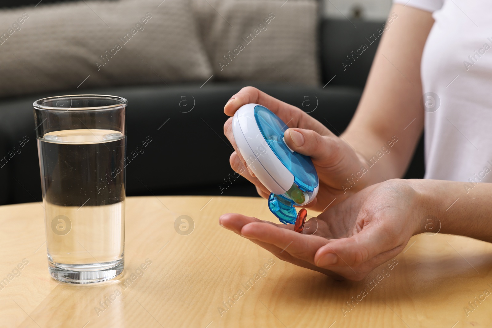 Photo of Woman with pills, organizer and glass of water at light wooden table, closeup