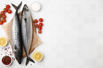 Photo of Raw mackerel, tomatoes and peppercorns on white tiled table, flat lay. Space for text