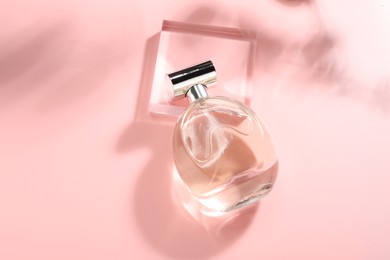 Photo of Bottle of luxury women's perfume in sunlight on pink background, above view