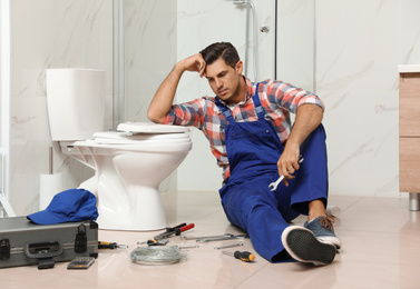 Professional plumber working with toilet bowl in bathroom