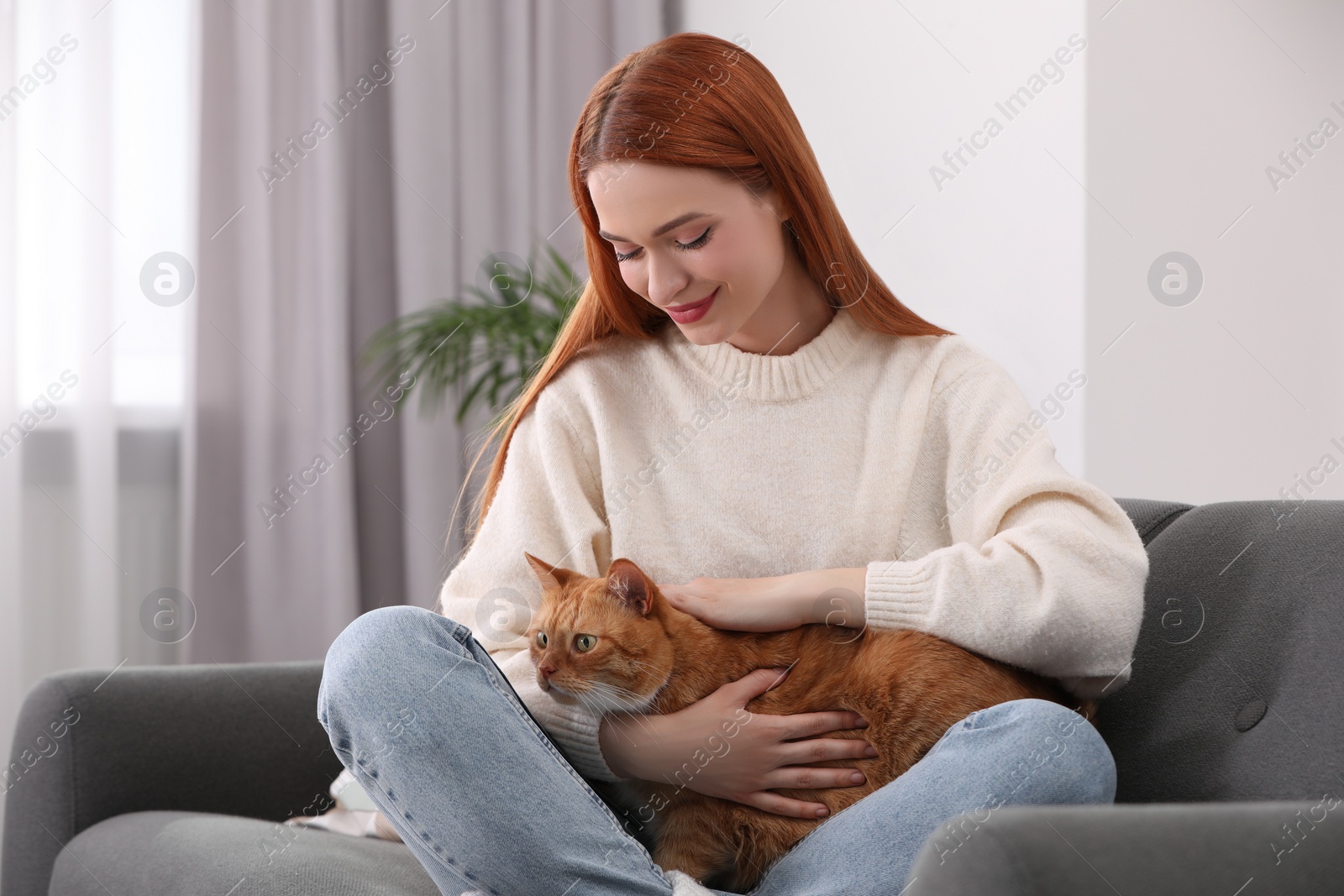 Photo of Woman stroking her cute cat on sofa at home