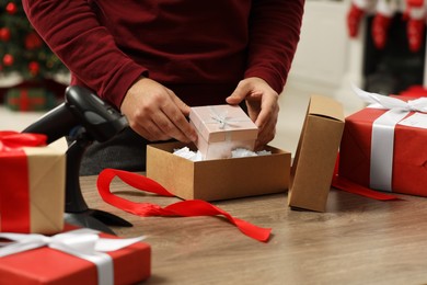 Man putting Christmas gift box into parcel at wooden table in post office, closeup