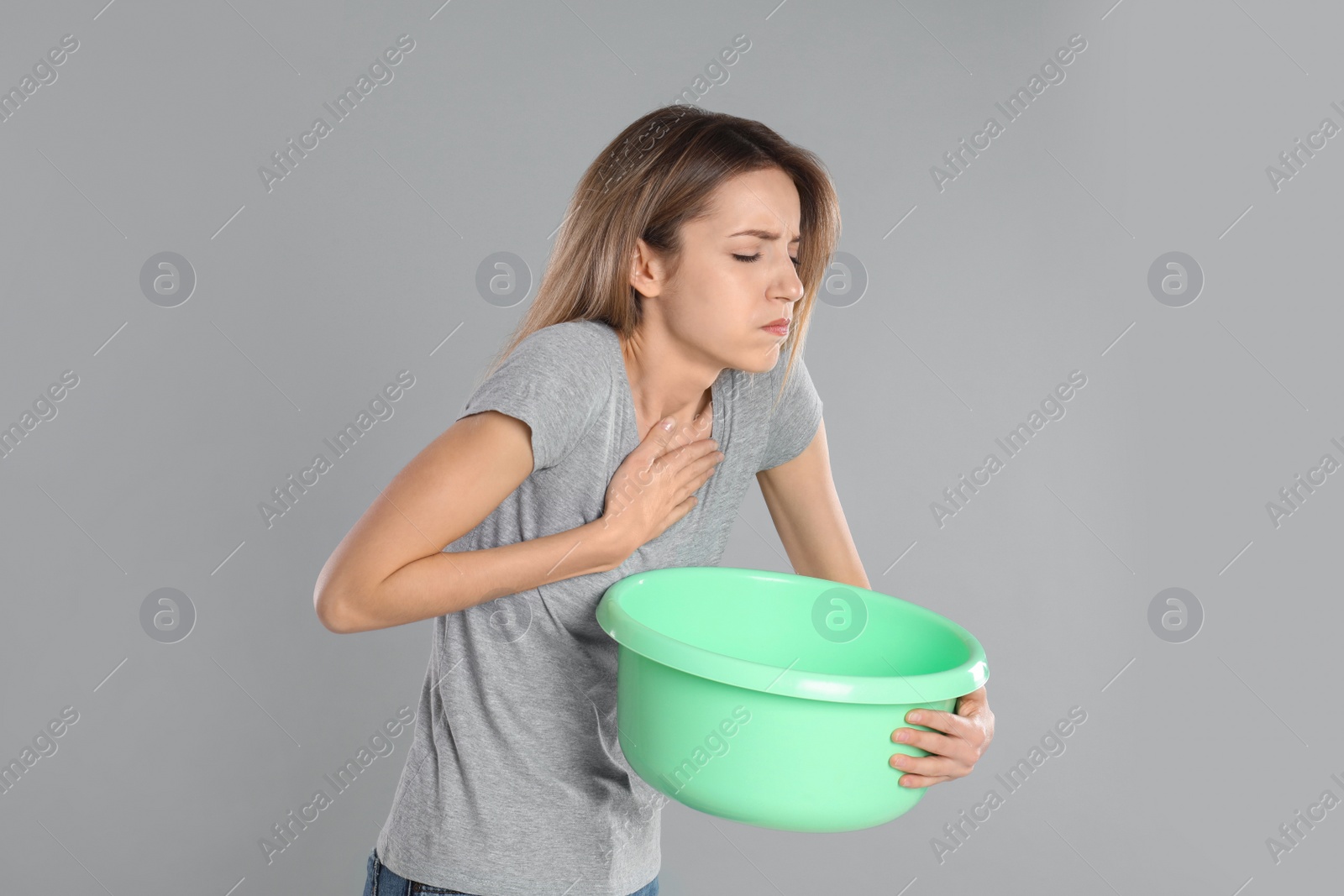 Photo of Woman with basin suffering from nausea on grey background. Food poisoning