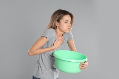 Woman with basin suffering from nausea on grey background. Food poisoning