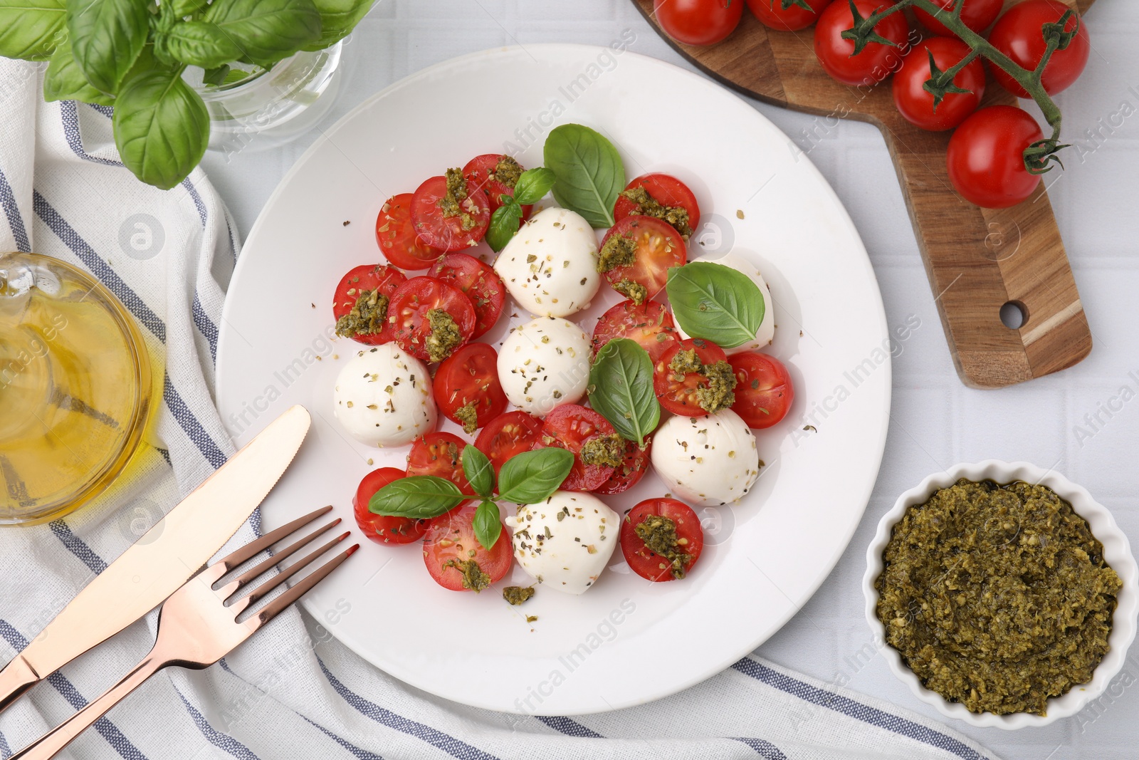 Photo of Tasty salad Caprese with tomatoes, mozzarella balls and basil served on white tiled table, flat lay