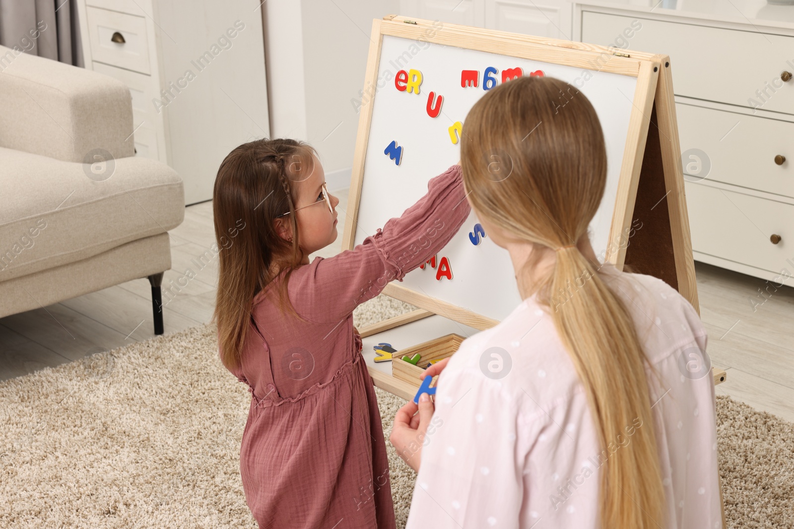 Photo of Mom teaching her daughter alphabet with magnetic letters at home