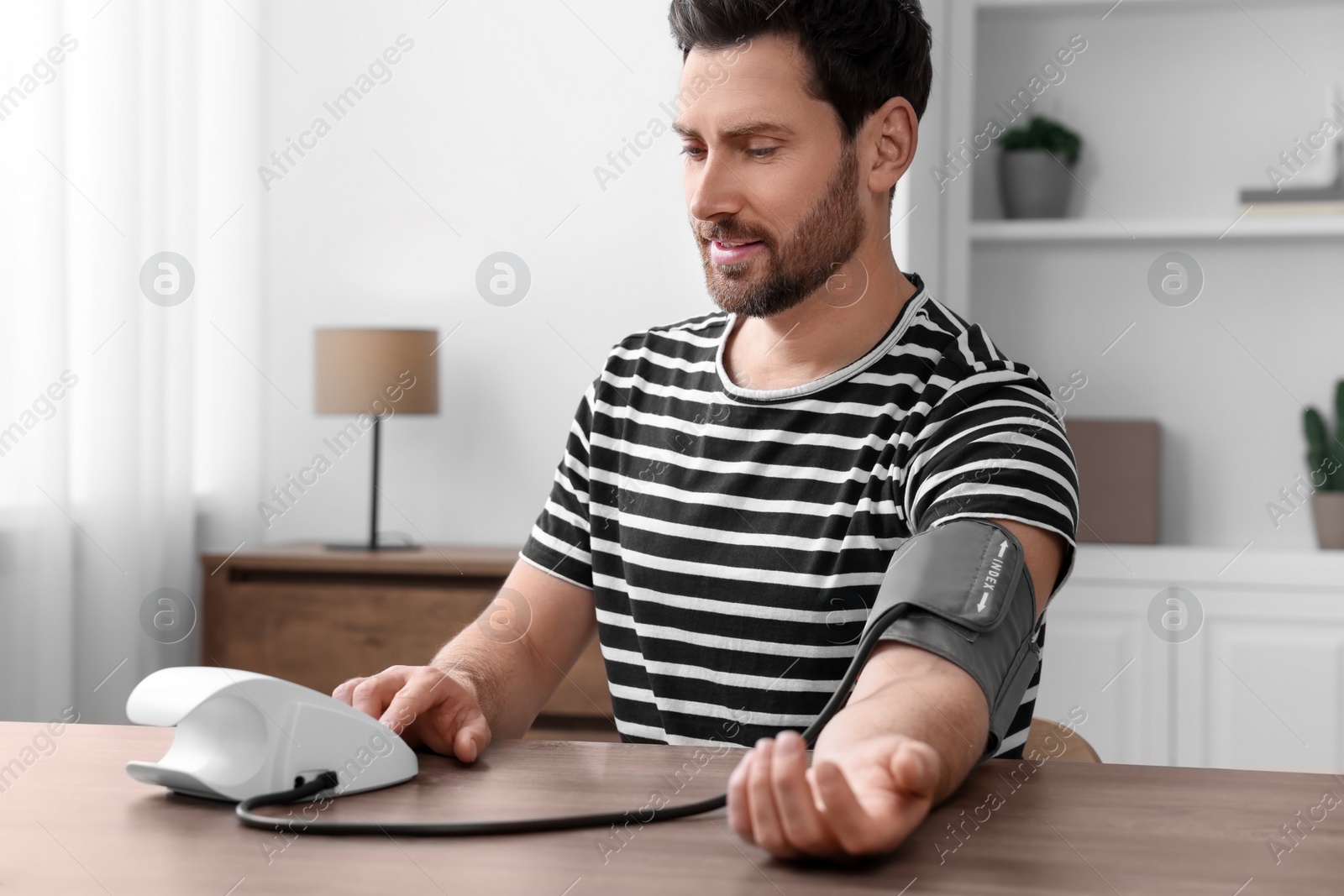 Photo of Man measuring blood pressure with tonometer in room